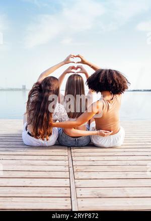 Tre adolescenti femminili di diversi gruppi etnici mostrano simboli del cuore con le mani Foto Stock