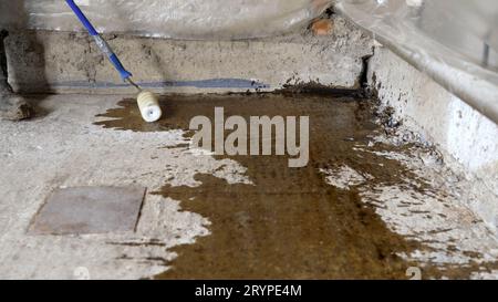 Processo di adescamento del pavimento. Un lavoratore applica un primer su un pavimento di cemento prima di posare un pavimento autolivellante. Primer per pavimenti in calcestruzzo per rafforzare Foto Stock