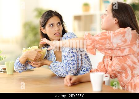 Donna che cerca di mangiare patatine fritte e amica egoista che evita a casa Foto Stock