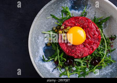 Tartaro gourmet di stile moderno crudo di filetto di manzo con uovo, rucola e capperi servito come vista dall'alto su un piatto di design con spazio per la copia a destra Foto Stock