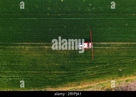 Immagine aerea del trattore con irroratrice di prodotto collegata in un campo di grano e prato, vista dall'alto con drone pov Foto Stock