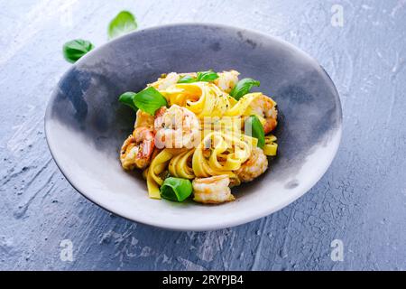 Le tradizionali tagliatelle italiane ai gamberoni, con gamberoni ed erbe, servite da vicino su un piatto di design con una copia del centro benessere Foto Stock