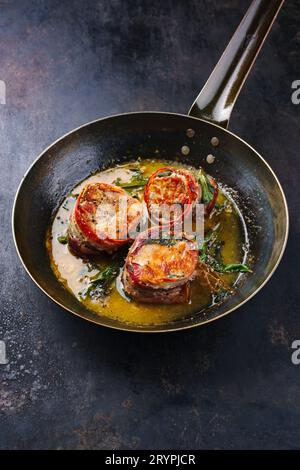 Tradizionali medaglioni di filetto di vitello arrosto con rivestimento di pancetta e foglie di salvia in salsa di burro serviti da vicino su un battuto rustico Foto Stock