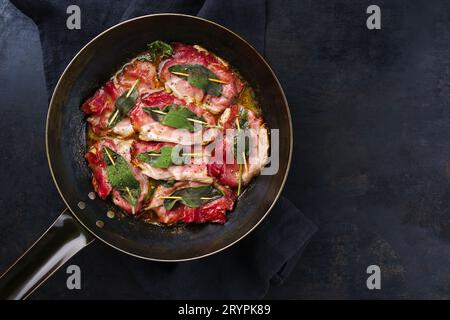 Tradizionale saltimbocca alla romana di maiale fritto italiano con prosciutto di Parma e foglie di salvia servita come vista dall'alto in una classica padella Foto Stock