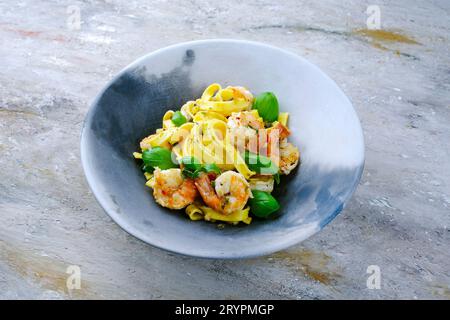 Le tradizionali tagliatelle italiane ai gamberoni, con gamberoni ed erbe, servite da vicino su un piatto di design con una copia del centro benessere Foto Stock