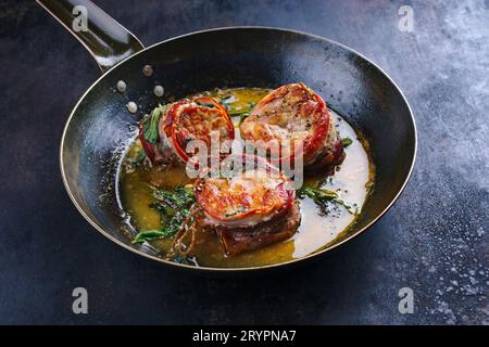 Tradizionali medaglioni di filetto di vitello arrosto con rivestimento di pancetta e foglie di salvia in salsa di burro serviti da vicino su un battuto rustico Foto Stock