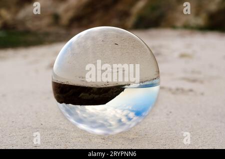 La lente a sfera di vetro si trova sulla sabbia della riva del mare Foto Stock