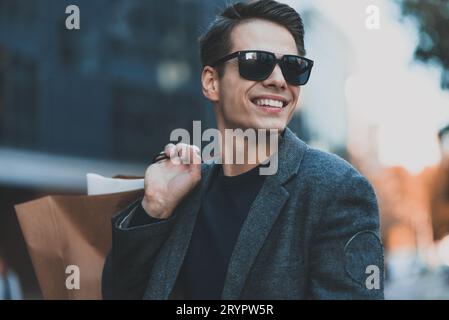 Felice giovane uomo di stile a piedi in via urbana e godendo lo shopping del Black Friday nei negozi alla moda in città. Foto Stock
