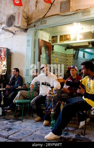 Giovani uomini seduti in un caffè della Medina, fumano tubi dell'acqua Foto Stock