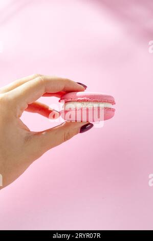 Ð¡perdere la mano di una donna che tiene macaron su sfondo rosa Foto Stock