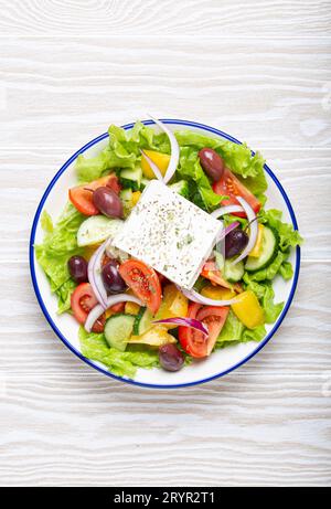 Insalata greca tradizionale con feta, pomodori, peperoni, cetrioli, olive, erbe in un recipiente di ceramica bianca su rustico bianco Foto Stock