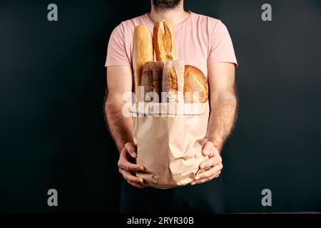 L'uomo tiene pani freschi di baguette di pane in sacchetto di carta su sfondo chiaro. Panetteria, concetto di cibo Foto Stock