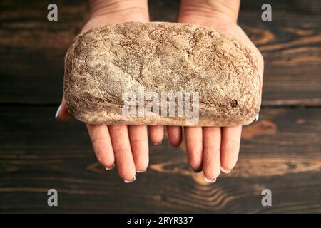 Pane multigrano di segale fresco in mani femminili su fondo di legno Foto Stock