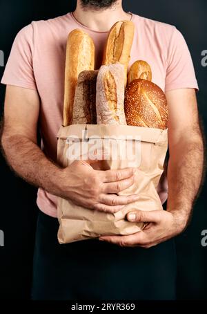 L'uomo tiene in sacchetto di carta delle baguette di pane fresche su sfondo chiaro Foto Stock