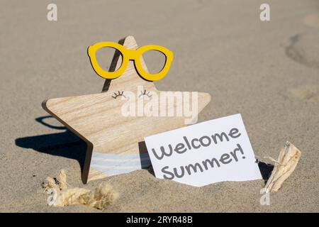 Testo DI BENVENUTO ESTIVO su carta biglietto d'auguri sullo sfondo di buffe stelle marine in bicchieri per le vacanze estive. Spiaggia sabbiosa Sun coa Foto Stock