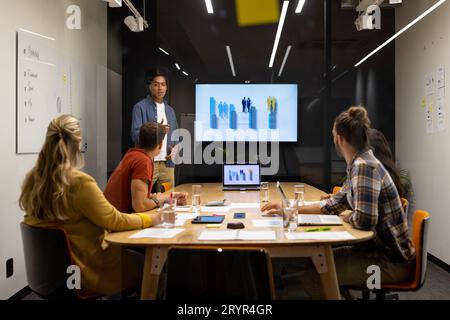 Creatività maschile birazziale che fa presentazioni sullo schermo a diversi colleghi nella sala riunioni Foto Stock