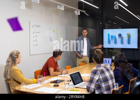 Creatività maschile birazziale che fa presentazioni sullo schermo a diversi colleghi nella sala riunioni Foto Stock