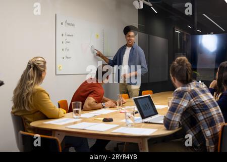 Presentazione creativa maschile birazziale alla lavagna bianca per diversi colleghi nella sala riunioni Foto Stock