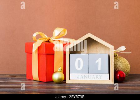 1 gennaio. Composizione natalizia su sfondo colorato con un calendario in legno, con una scatola regalo, giocattoli, spazio copia capiente. Foto Stock