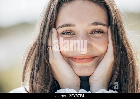 Bella e felice ragazza che tiene le guance con una risata, guardando la telecamera. Bella giovane donna pulita pelle fresca . fa espressivo Foto Stock