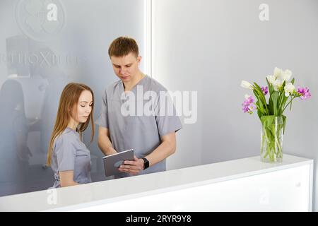 Dentista con infermiera dentale in moderno studio dentale usando il pc della compressa che indossa uniforme. Specialista ortodontico e assistente alla reception in clinica dentale d Foto Stock