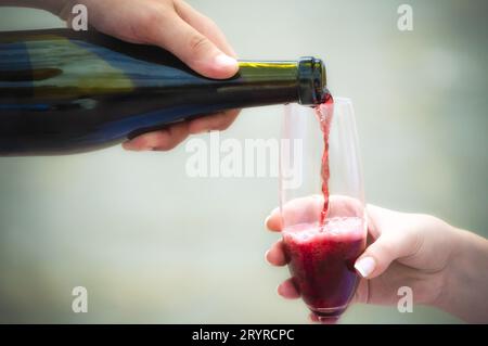 L'uomo versa vino rosso da una bottiglia in un bicchiere nella mano di una donna Foto Stock