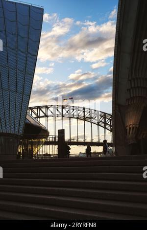 Sydney Harbour Bridge che sorvola la bandiera aborigena australiana e la bandiera australiana, pomeriggio visto tra le conchiglie della Sydney Opera House Foto Stock