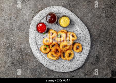 Calamari fritti anelli in pietra grigia piastra con salse. Grigio sfondo concreto Foto Stock