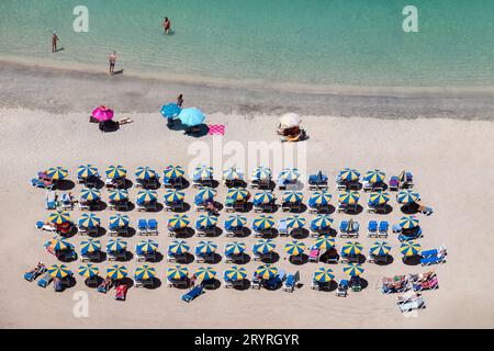 I vacanzieri si rilassano su una spiaggia soleggiata ad Amadores, Gran Canaria, Spagna. Le sedie a sdraio sono sistemate in modo ordinato sotto ombrelloni colorati vicino al mare Foto Stock