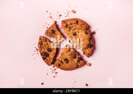 Biscotti e briciole di cioccolato rotti su sfondo rosa Foto Stock