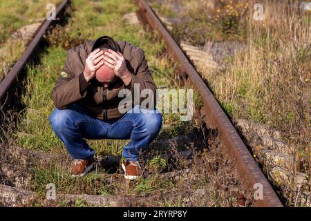 L'uomo premuroso siede su binari. La persona sconvolta in uno stress. Stress concettuale, fallimento della vita, problema. Triste maschio Foto Stock