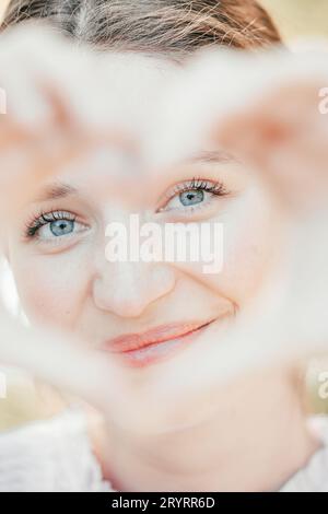 Immagine ravvicinata di una donna sorridente in natura che forma il cuore con le mani. Bella donna caucasica gioiosa che ride alla macchina fotografica Foto Stock