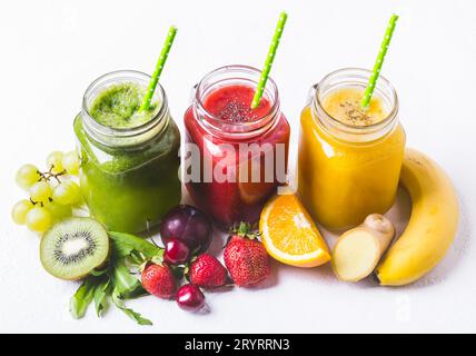 Frullato rosso, giallo e verde in un vaso di vetro e ingredienti su sfondo bianco Foto Stock