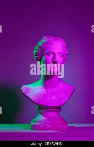 Copia in gesso del busto in gesso di antica statua, Venere sullo sfondo viola dello studio con luci al neon. Concetto di arte e mitologia Foto Stock