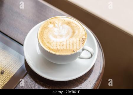Tazza bianca di cappuccino con crema fine su un tavolo di legno in caffetteria Foto Stock