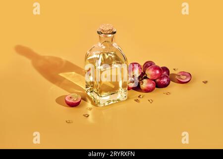 Olio di semi d'uva in bottiglia e grappolo d'uva su sfondo giallo e ombre alla moda. Riutilizzare i rifiuti alimentari Foto Stock