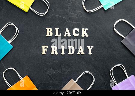Testo in legno Black friday e sacchetti di carta su sfondo nero testurizzato, vista dall'alto. Foto Stock