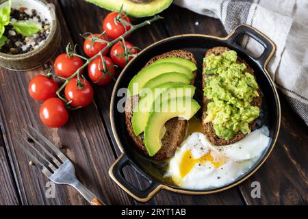 Pane tostato integrale con avocado a fette e uova in camicia su un tavolo rustico. Colazione sana, panino con avocado e uova. Foto Stock