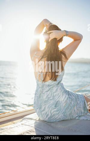 Una giovane donna con un bellissimo ed elegante abito da sole siede sul ponte di una nave e incontra l'alba Foto Stock