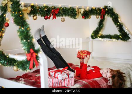 Ragazza dai capelli rossi sdraiata su un letto e regge un regalo di Natale Foto Stock