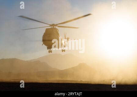 Un elicottero militare è visto volare e atterrare nel deserto al tramonto in una nuvola di polvere. Aerei dell'aeronautica Foto Stock