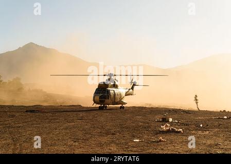 Un elicottero militare è visto volare e atterrare nel deserto al tramonto in una nuvola di polvere. Aerei dell'aeronautica Foto Stock