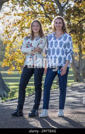 Due giovani donne, amici, condividono la conversazione sotto i torreggianti alberi autunnali, retroilluminati dal sole del pomeriggio Foto Stock
