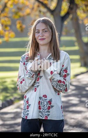 Sotto gli alberi autunnali, una giovane donna indossa la camicia mentre guarda la fotocamera Foto Stock