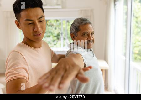 Fisioterapista maschile felice eterogeneo e paziente anziano che tende il braccio Foto Stock