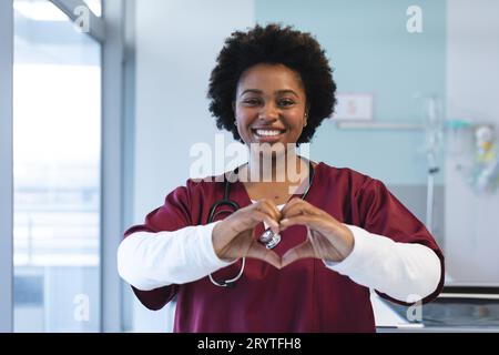 Ritratto di una felice dottoressa afro-americana che indossa scrub, che forma le mani a forma di cuore Foto Stock
