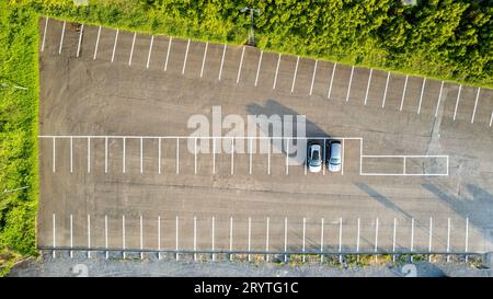 Vista aerea di un parcheggio quasi vuoto con due auto parcheggiate all'alba, che proiettano lunghe ombre. Foto Stock