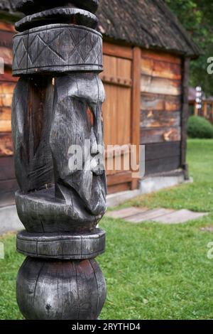 Postazione di aggancio sullo sfondo della casa di servizio. Scolpito da un tronco a forma di faccia di un idolo di legno. Foto Stock