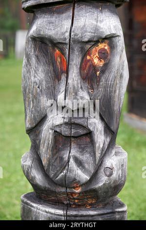 Postazione di aggancio sullo sfondo della casa di servizio. Scolpito da un tronco a forma di faccia di un idolo di legno. Foto Stock