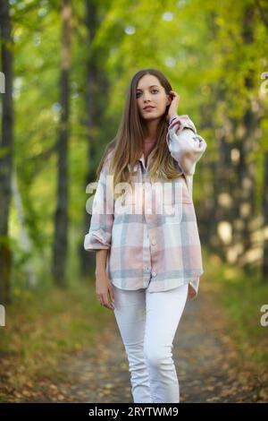 Donna bionda in abito informale che cammina lungo il vicolo autunnale degli alberi di tiglio. Foto Stock